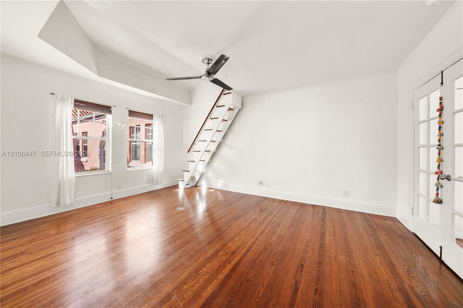 Hardwood flooring, vaulted ceiling, multi-pane French doors, ceiling fan, and architectural staircase