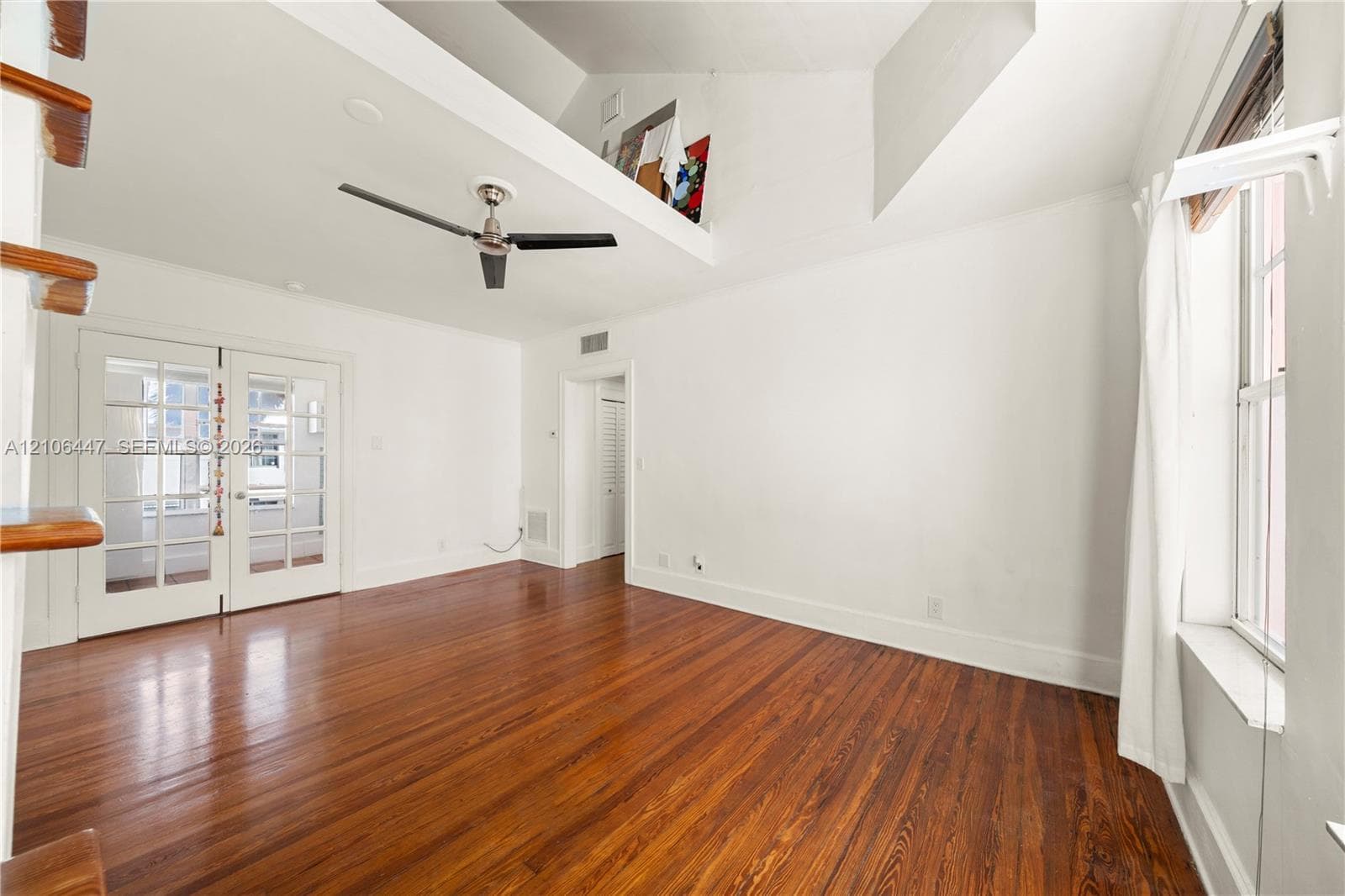 Vaulted ceiling with an integrated loft area, wood-finish flooring, multi-pane glass double doors, and a ceiling fan