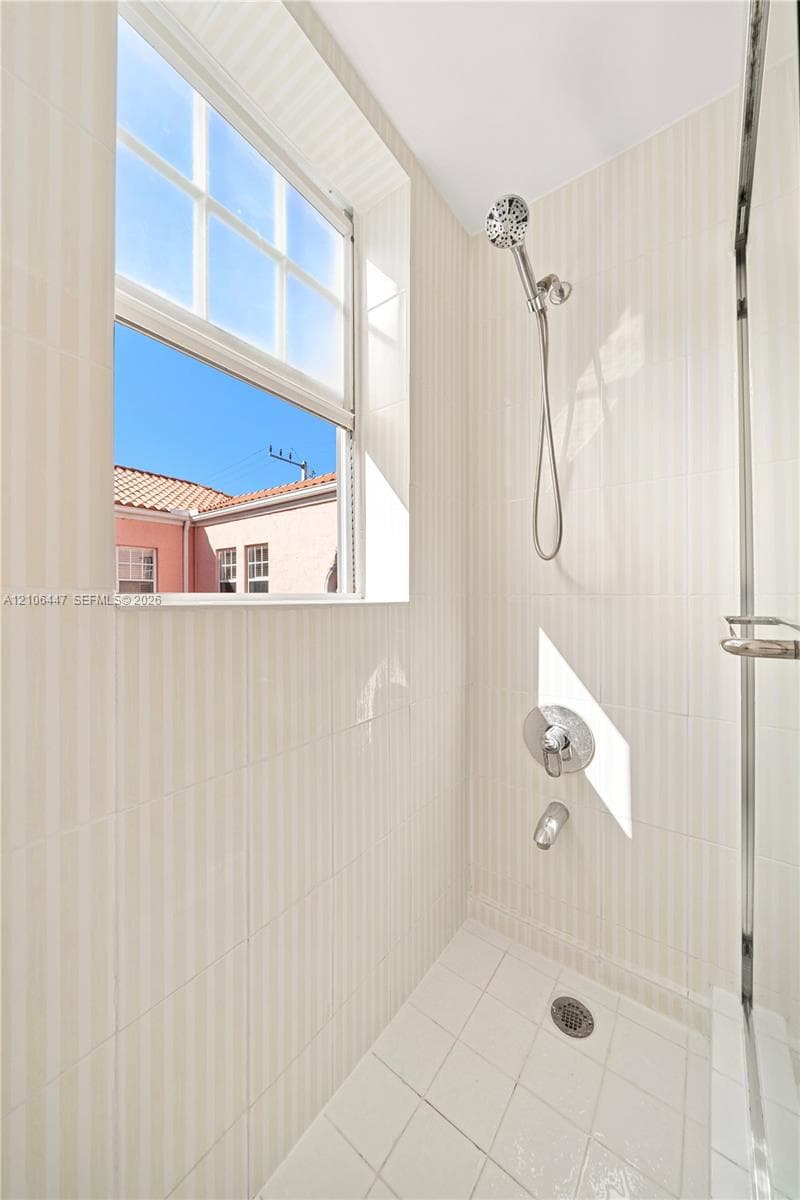 Shower enclosure featuring floor-to-ceiling vertical ceramic wall tile, a hand-held shower head, chrome fixtures, and a recessed window