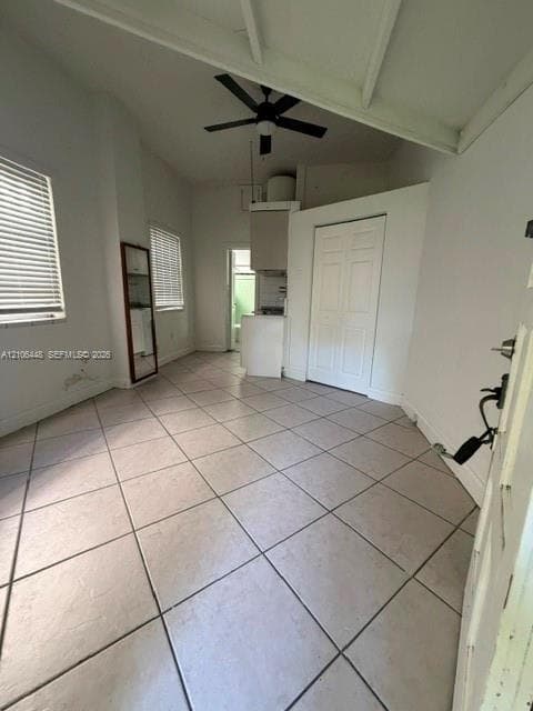 Interior space featuring vaulted ceilings, neutral ceramic tile flooring, a ceiling fan, and double-panel closet doors