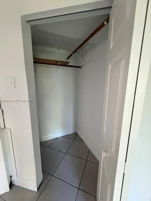 Storage closet featuring neutral floor tile, a built-in shelf, and a hanging rod