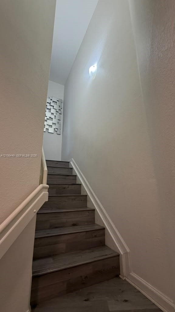 Staircase featuring wood-finish treads and a wall-mounted handrail