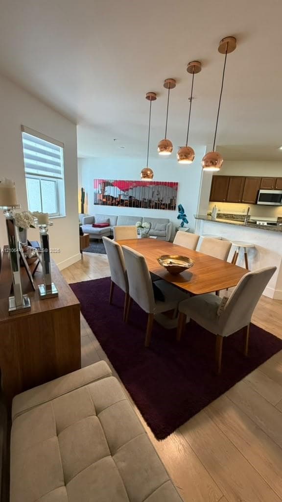 Open concept area featuring wood-finish flooring, four brushed-metal pendant lights, and kitchen cabinetry with a breakfast bar