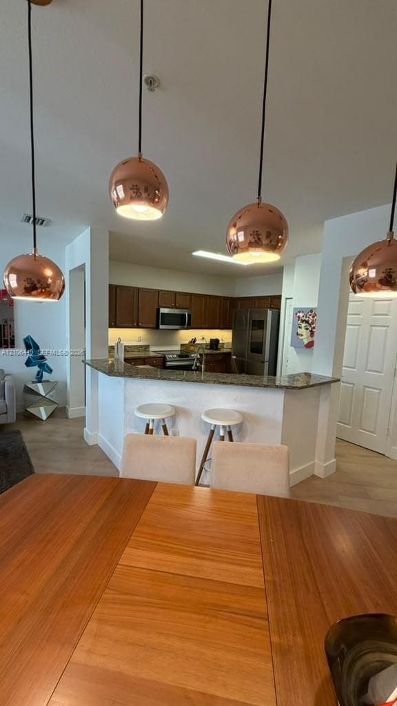 Kitchen featuring polished stone countertops, dark wood-finish cabinetry, stainless steel appliances, and four metallic spherical pendant lights