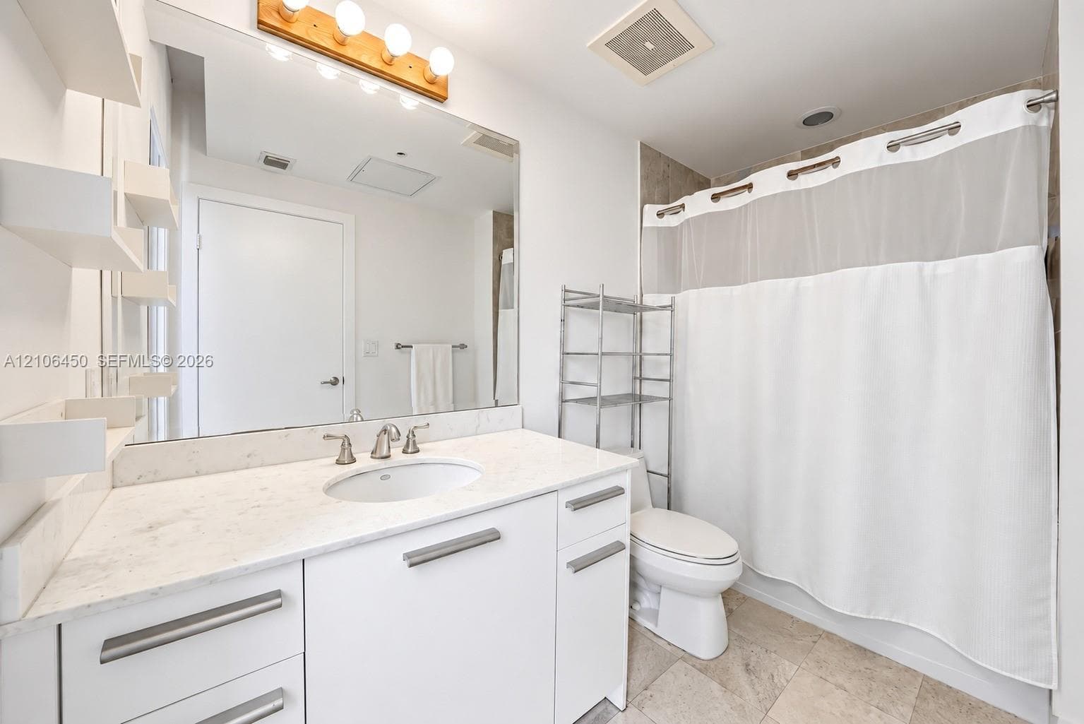 Bathroom featuring a white vanity with integrated stone countertop and undermount sink, large wall-mounted mirror, wood-finish light fixture, and stone tile flooring