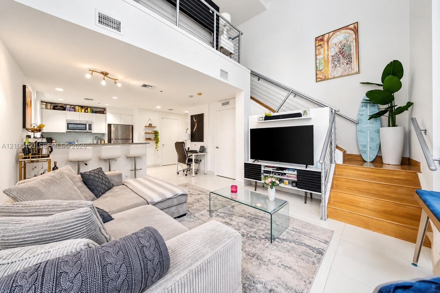 Open-concept interior featuring high ceilings, stainless steel kitchen appliances, wood-tread stairs, and metal cable railing