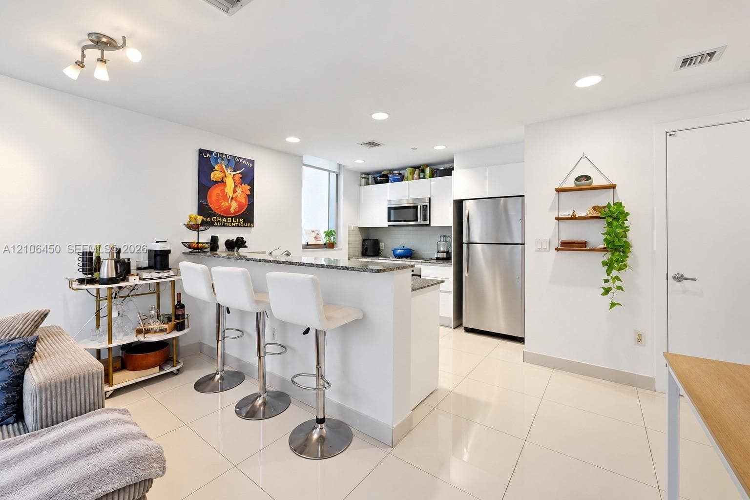Kitchen featuring white cabinetry, stone countertops, a breakfast bar, stainless steel appliances, and large-format tile flooring