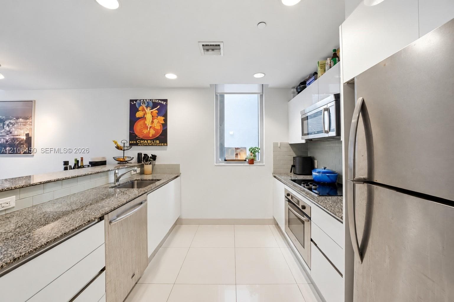 Kitchen featuring white flat-panel cabinetry, stone countertops, stainless steel appliances, and large-format tile flooring