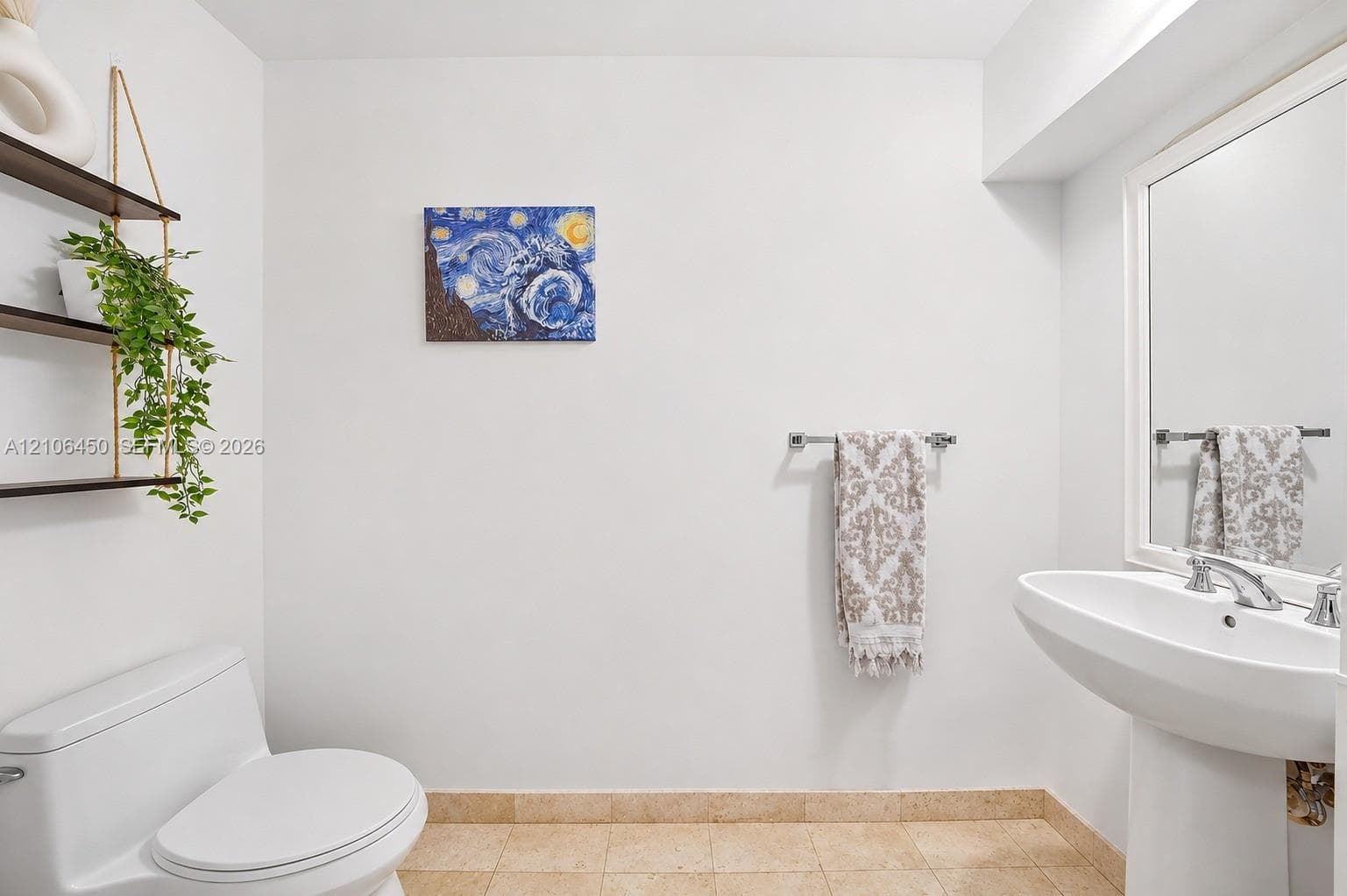 Wall-mounted open shelving with dark wood finish, pedestal sink with chrome faucet, large rectangular mirror with white frame, and stone-tile flooring