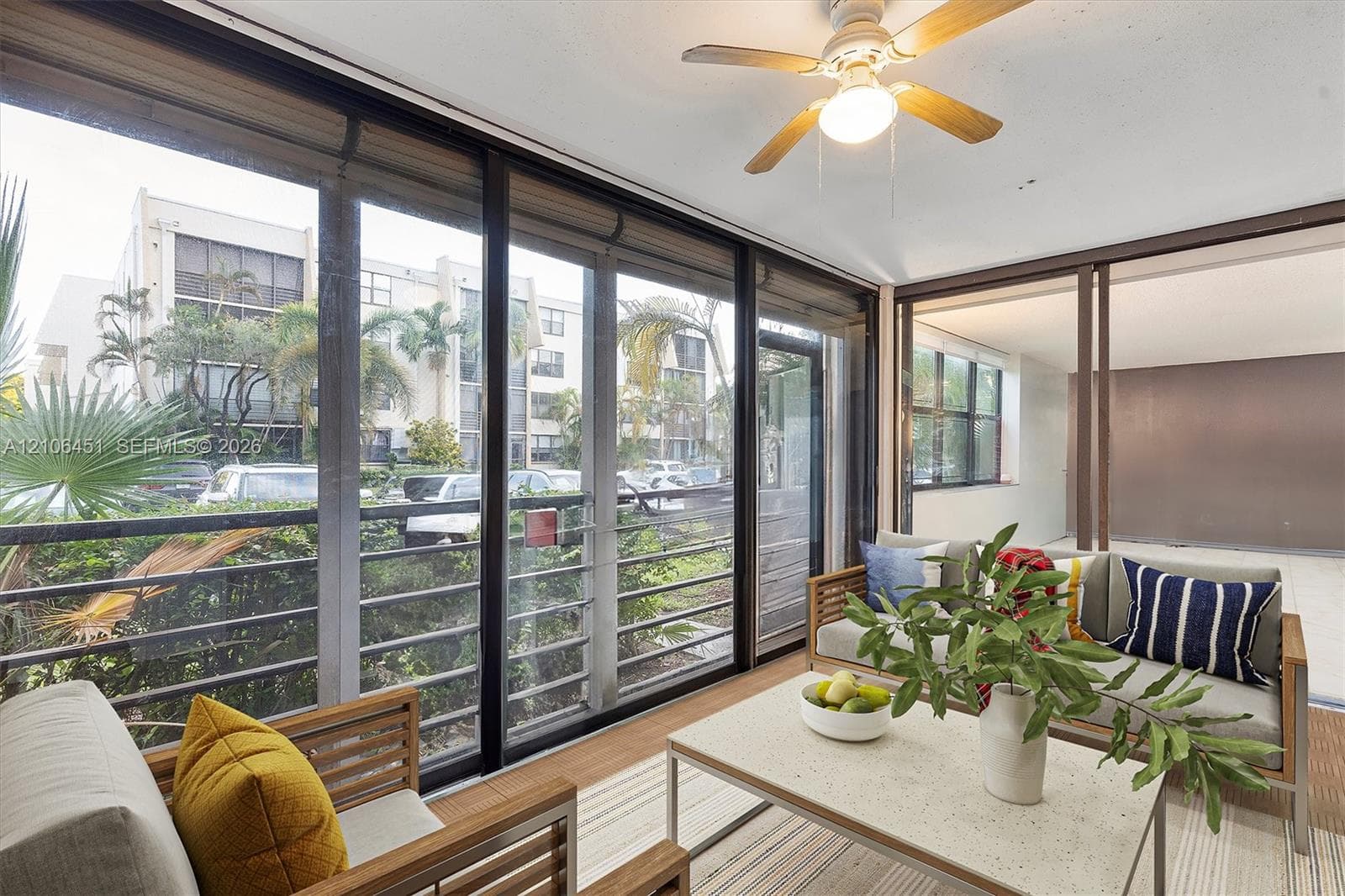 Enclosed patio featuring expansive floor-to-ceiling sliding glass doors, neutral wood-finish flooring, and a ceiling-mounted fan with integrated lighting