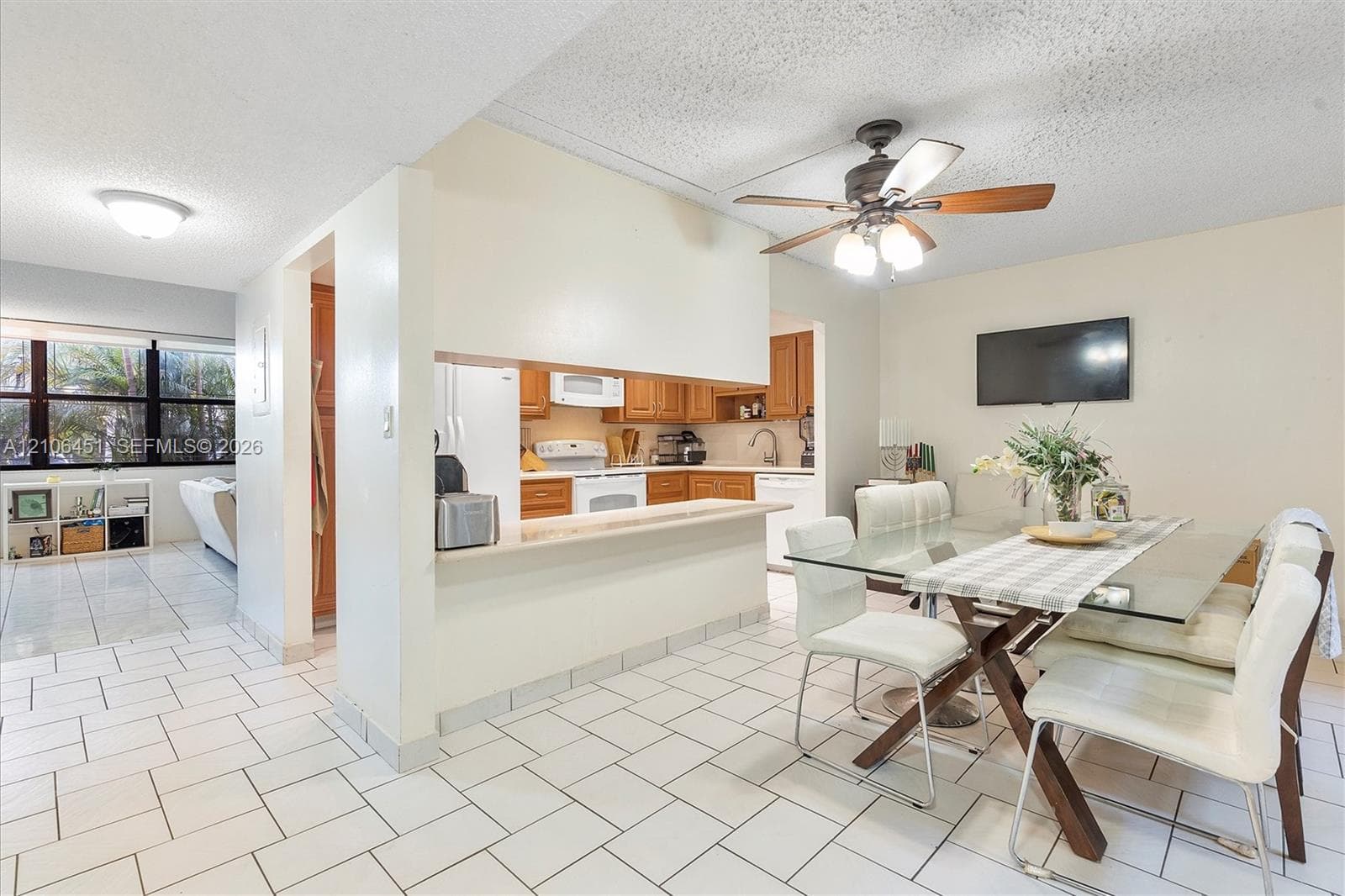 Dining area featuring ceramic tile flooring, a central ceiling fan with integrated lighting, and an open kitchen pass-through with a breakfast bar