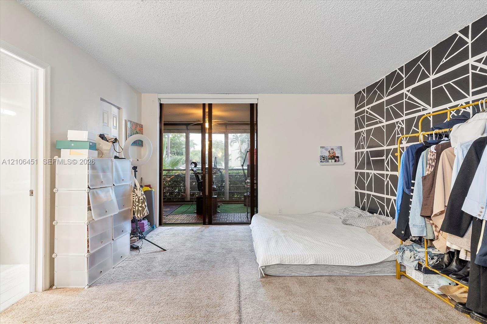 Neutral wall-to-wall carpeting, geometric patterned accent wall, and sliding glass doors with access to a private screened balcony