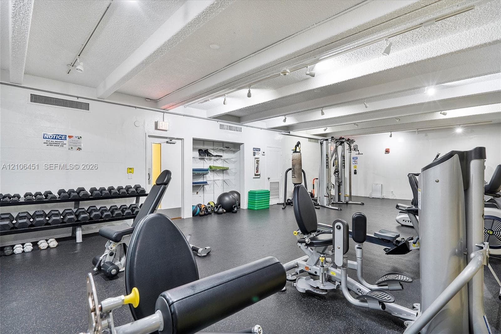 Fitness center featuring industrial-style exposed ceiling beams, track lighting, rubberized flooring, and built-in recessed shelving