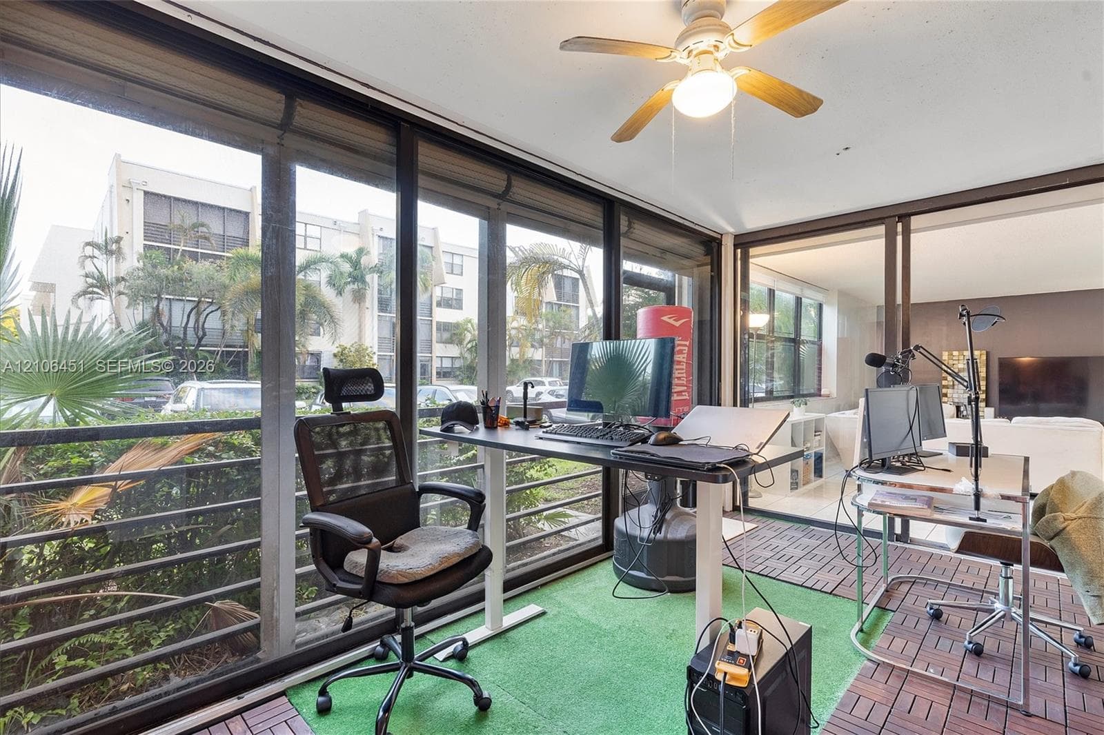 Enclosed sunroom featuring floor-to-ceiling windows, interlocking wood-finish patio tiles, and a ceiling fan with integrated lighting