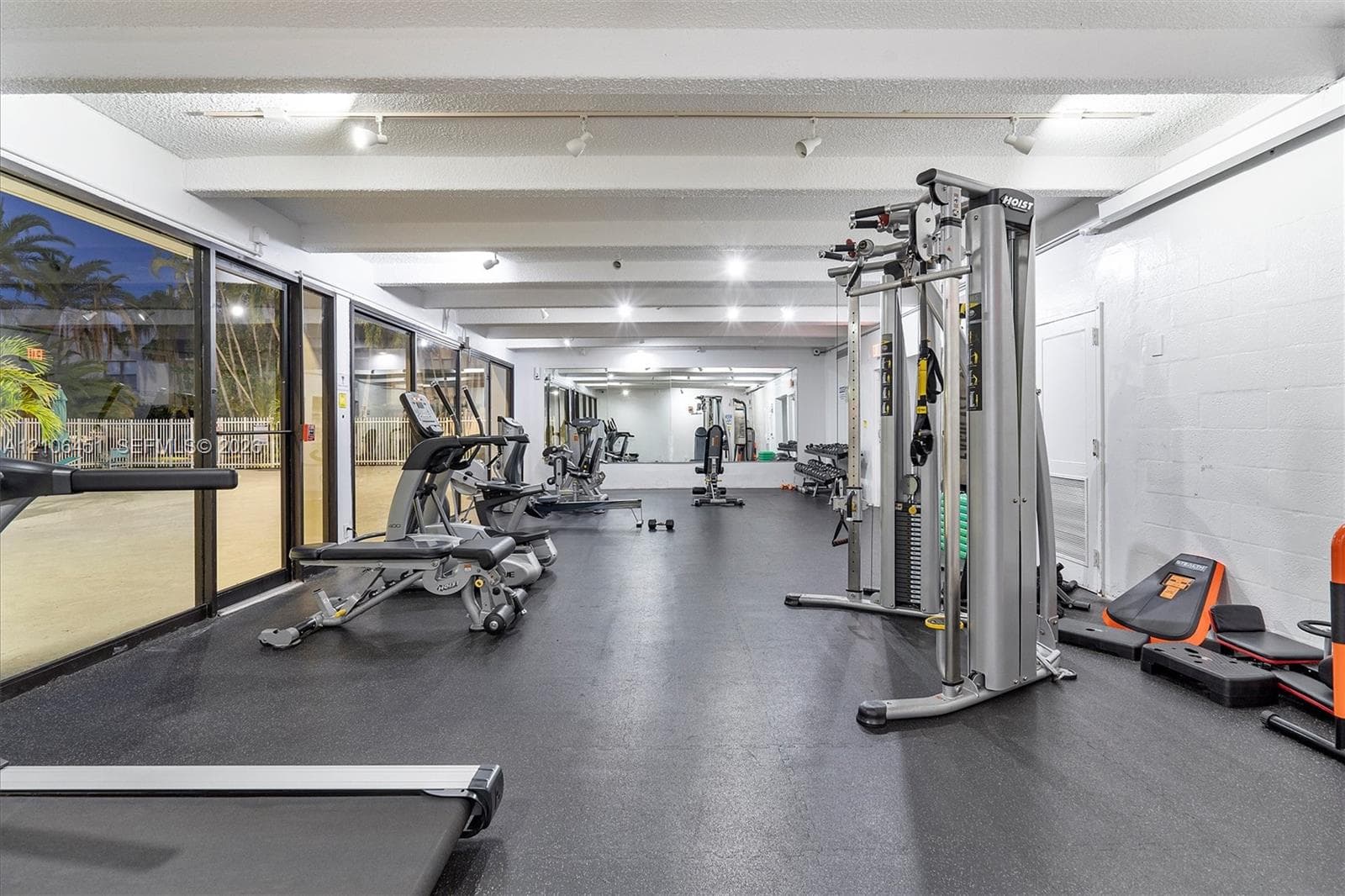 Fitness center featuring rubber flooring, floor-to-ceiling glass panels, exposed painted structural beams, and wall-mounted track lighting