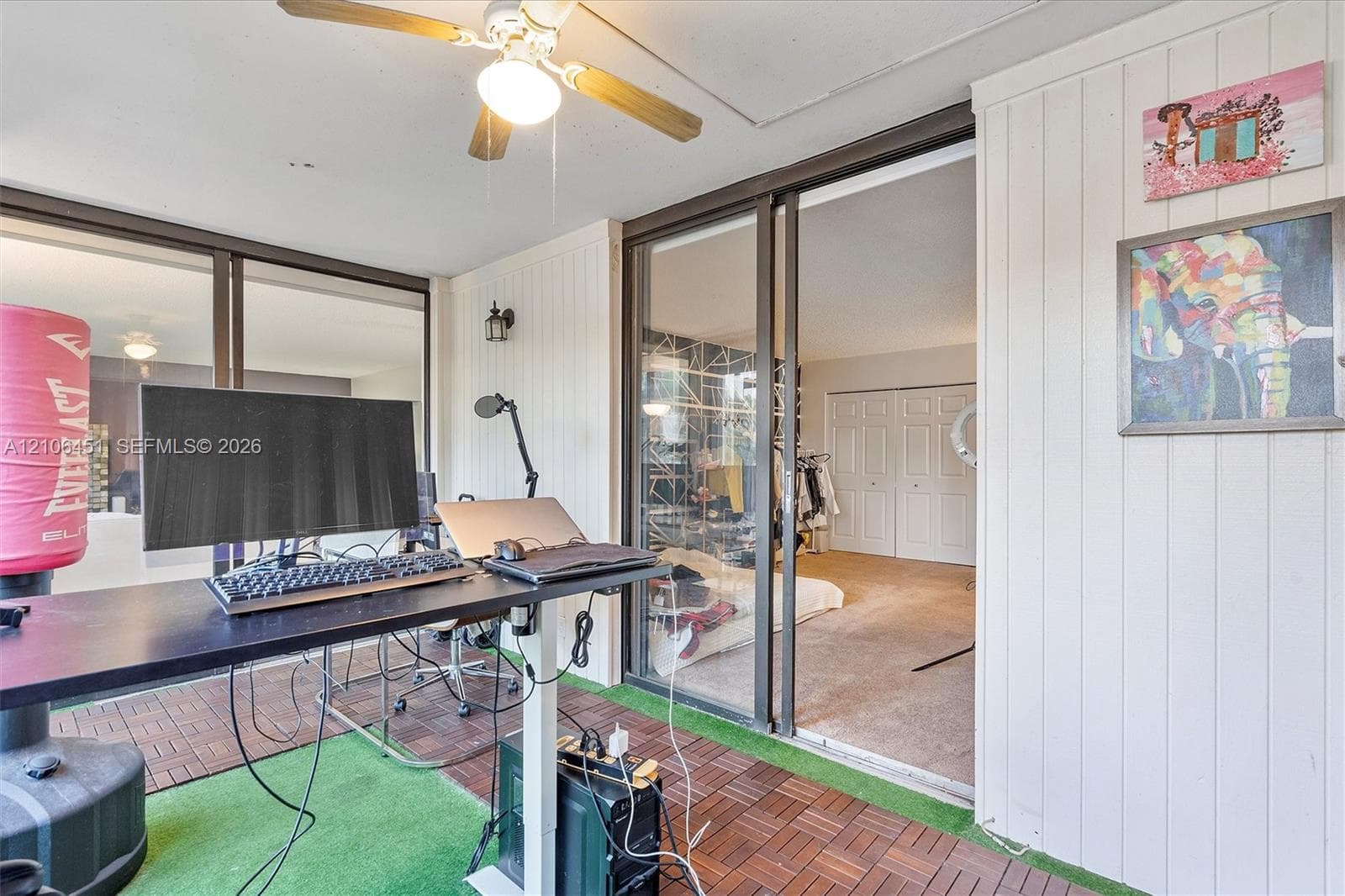 Enclosed patio featuring multi-panel sliding glass doors, vertical panel siding, recessed lighting, and interlocking wood-finish patio tiles