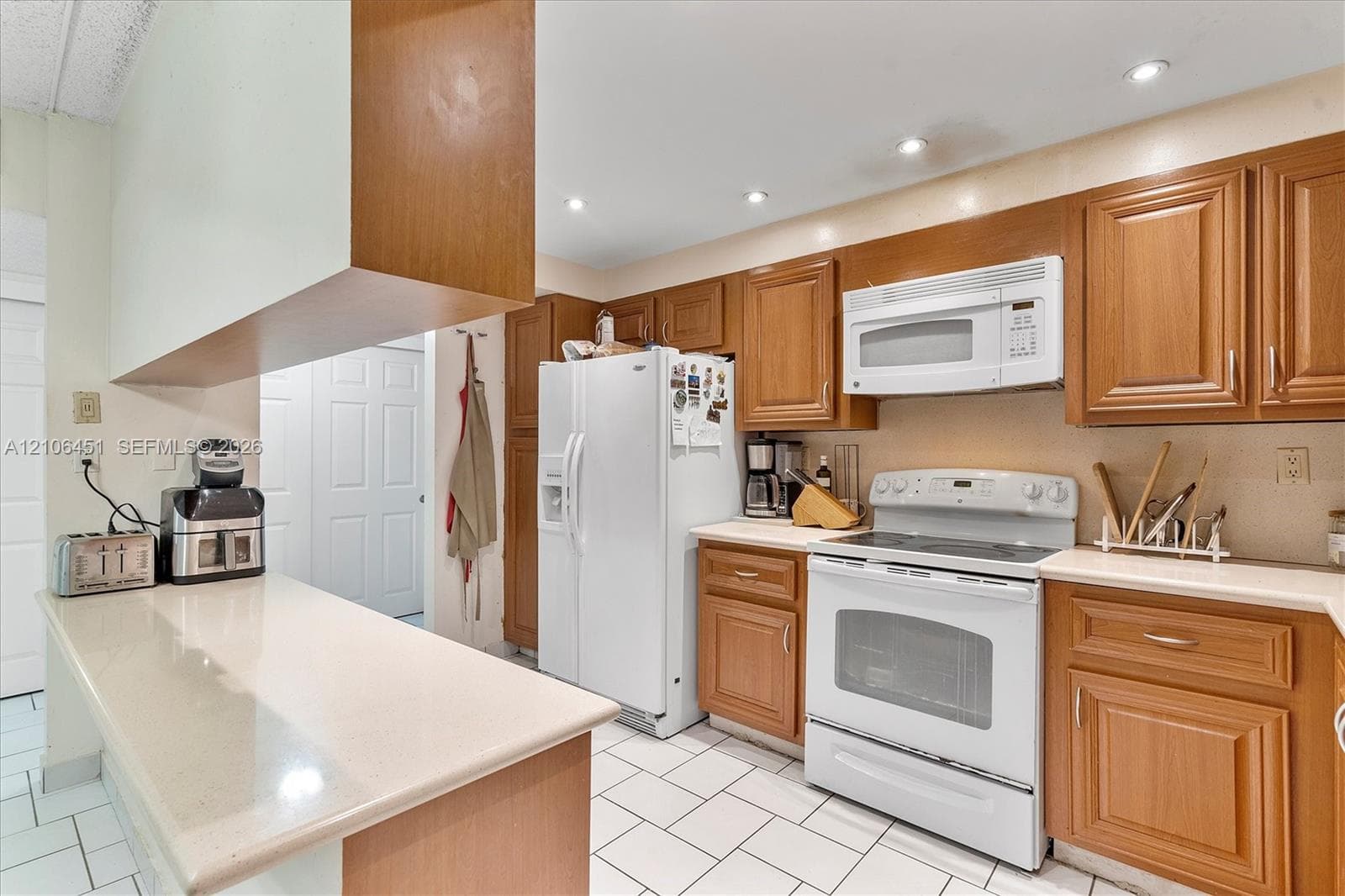 Kitchen featuring wood cabinetry, white tile flooring, recessed lighting, solid-surface countertops, and white appliances