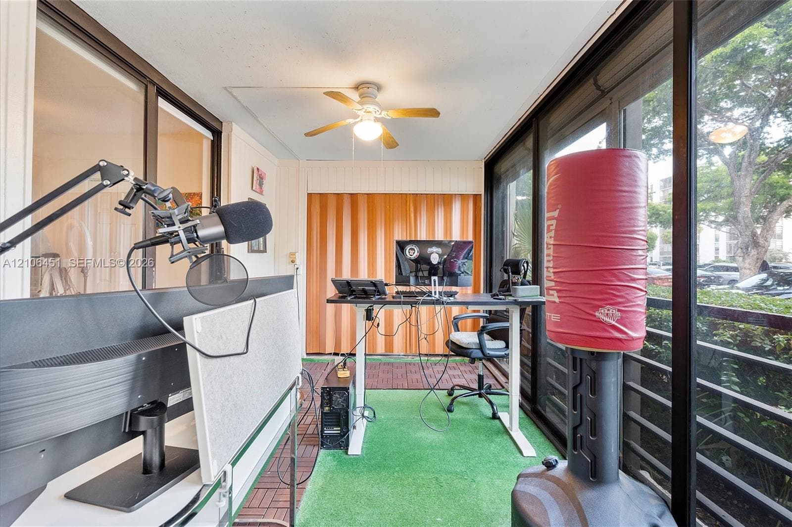 Enclosed sunroom featuring floor-to-ceiling sliding glass panels, vertical wood-panel accent wall, and a ceiling-mounted light fixture with fan