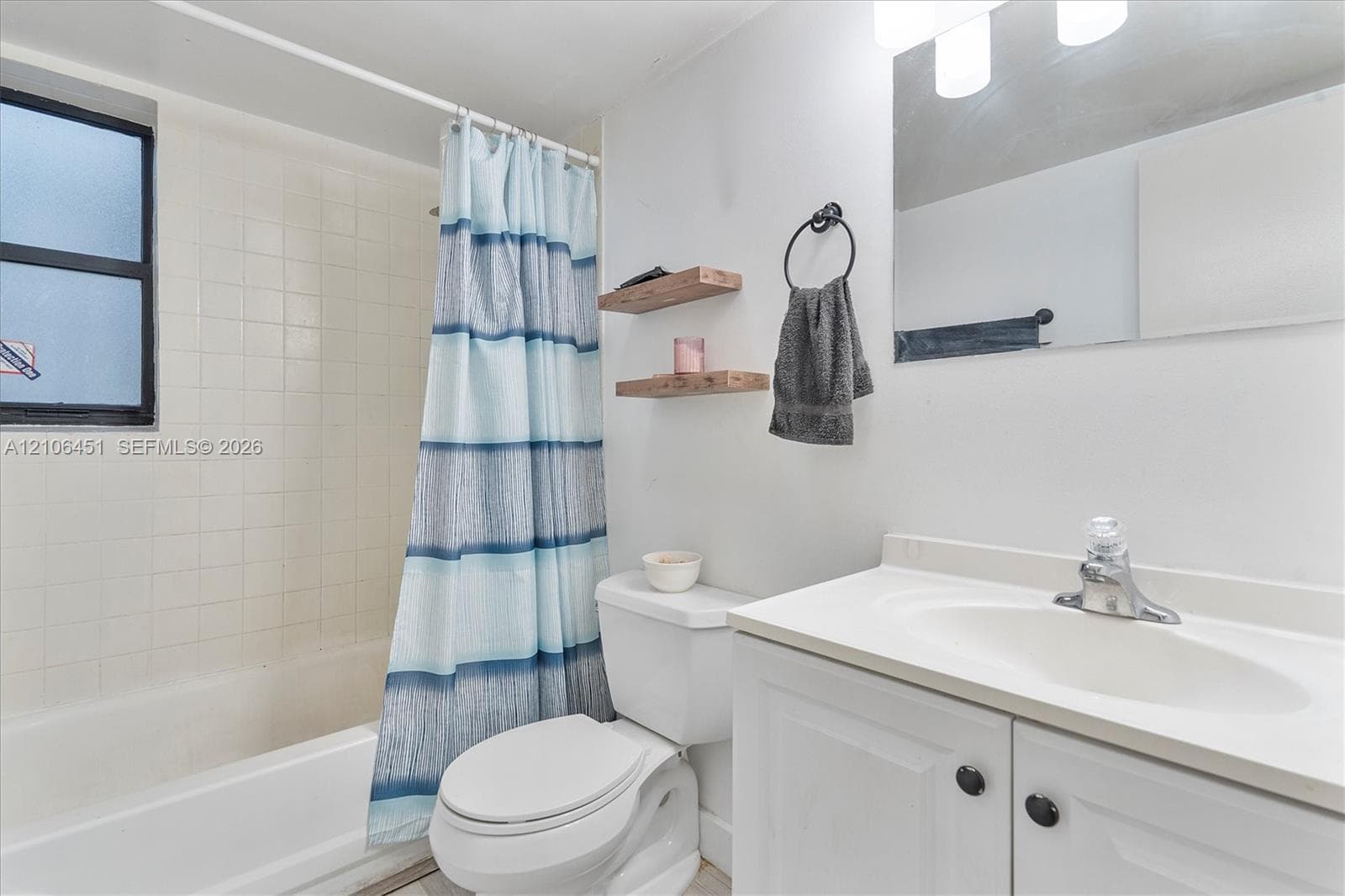 Bathroom featuring a white vanity cabinet with an integrated sink, a rectangular wall-mounted mirror, a tub-shower combination with tile surround, and dual wall-mounted floating shelves