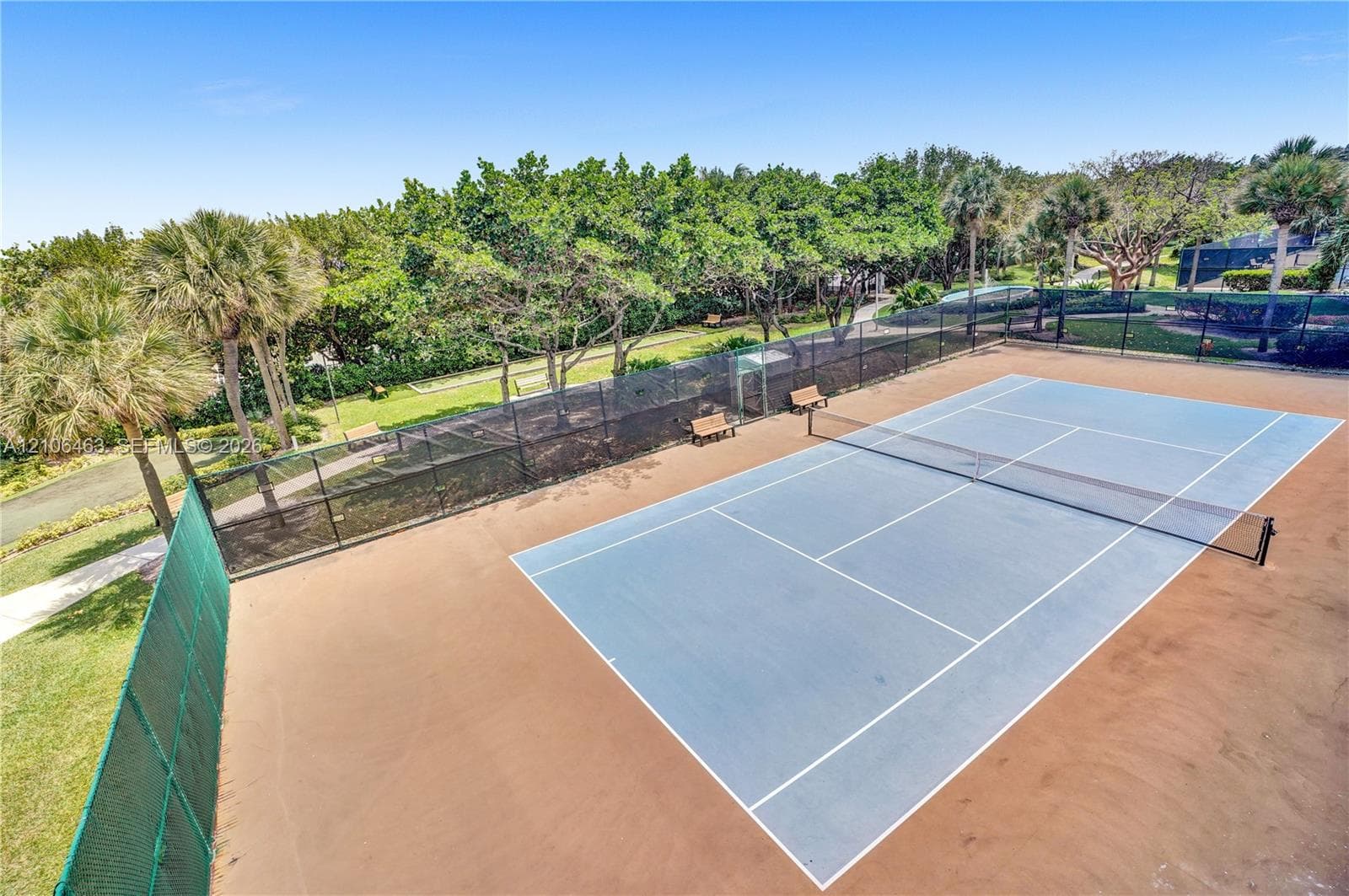 Tennis court featuring a blue hard-surface finish, perimeter chain-link fencing, and integrated net