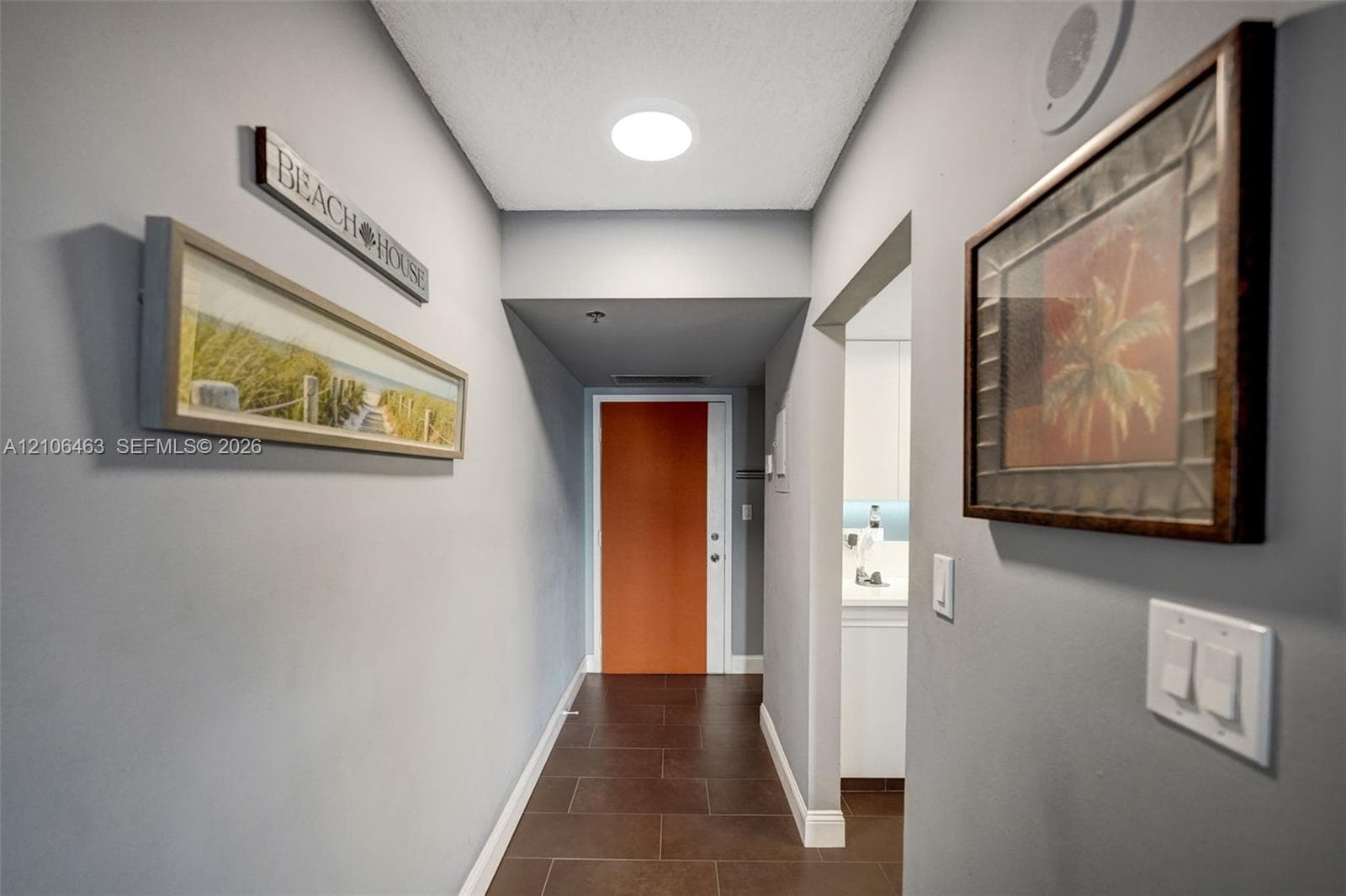Hallway featuring large-format ceramic tile flooring, neutral grey wall paint, and a bold orange solid-core entry door