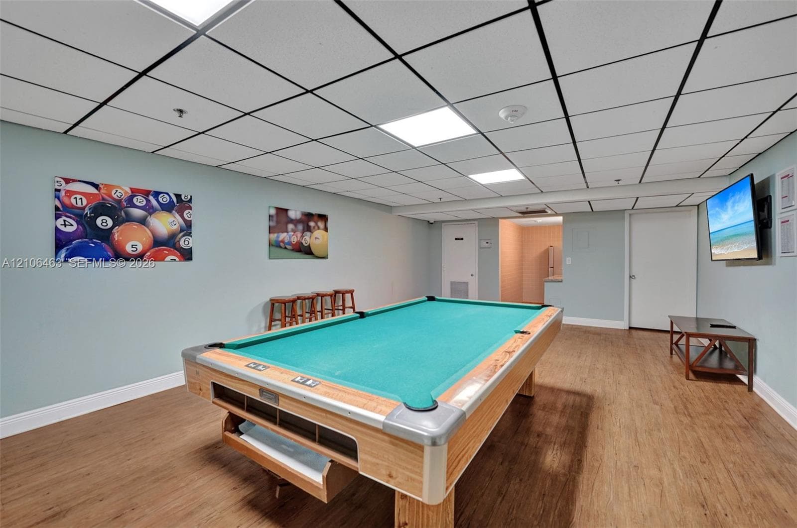 Finished recreation room featuring wood-finish flooring, a drop ceiling with recessed panel lighting, and solid-core interior doors