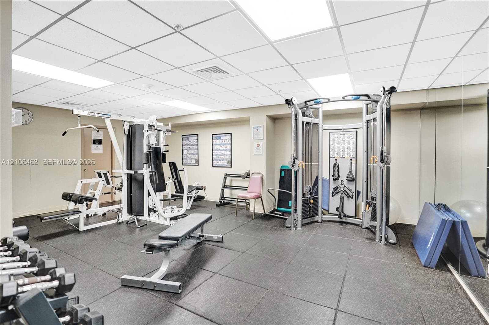 Fitness area featuring durable rubberized flooring, mirrored wall panels, and drop ceiling with recessed lighting
