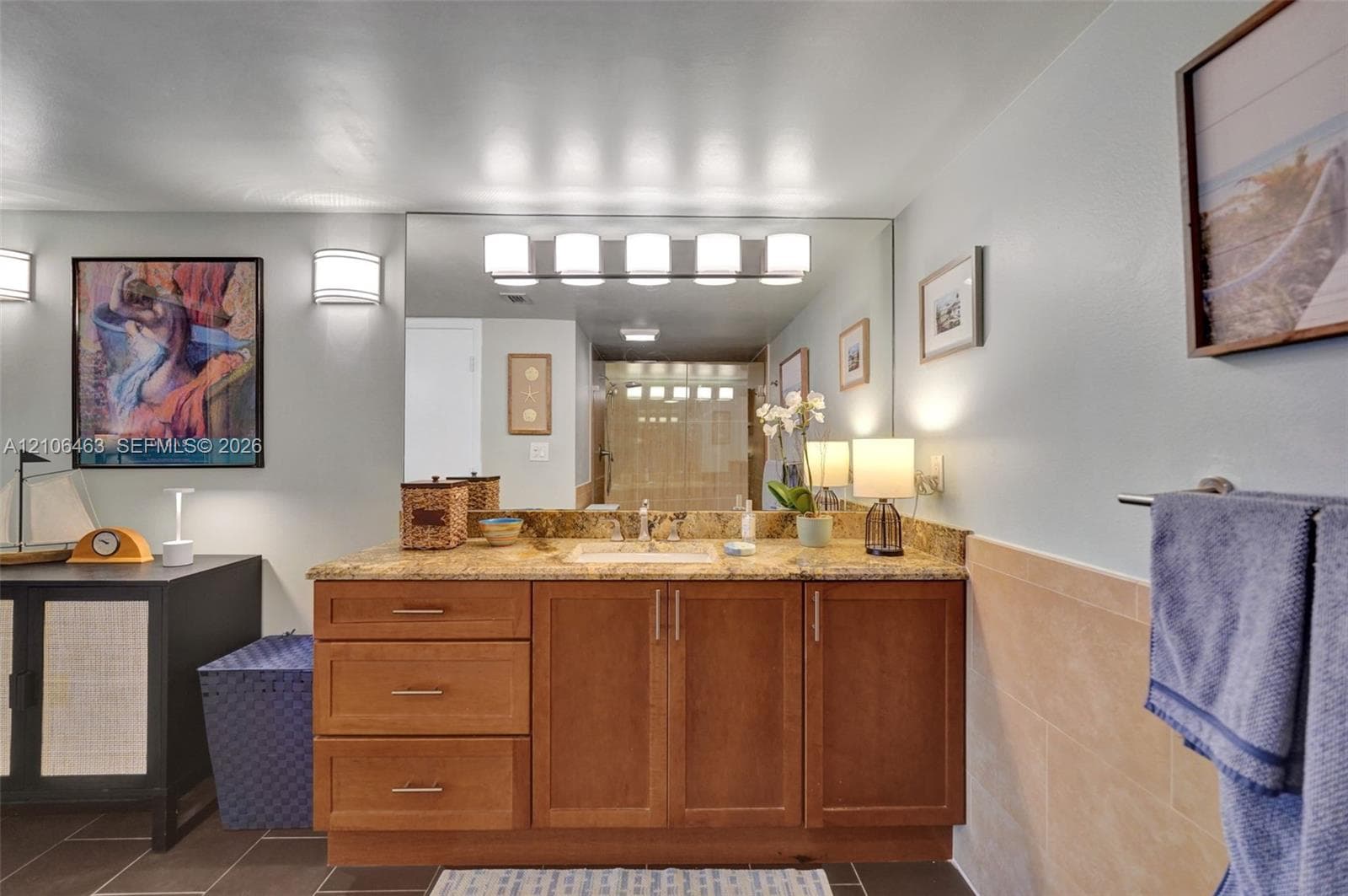 Wood-finish vanity cabinetry with an integrated countertop, large wall-mounted vanity mirror, five-light fixture, and ceramic tile wainscoting