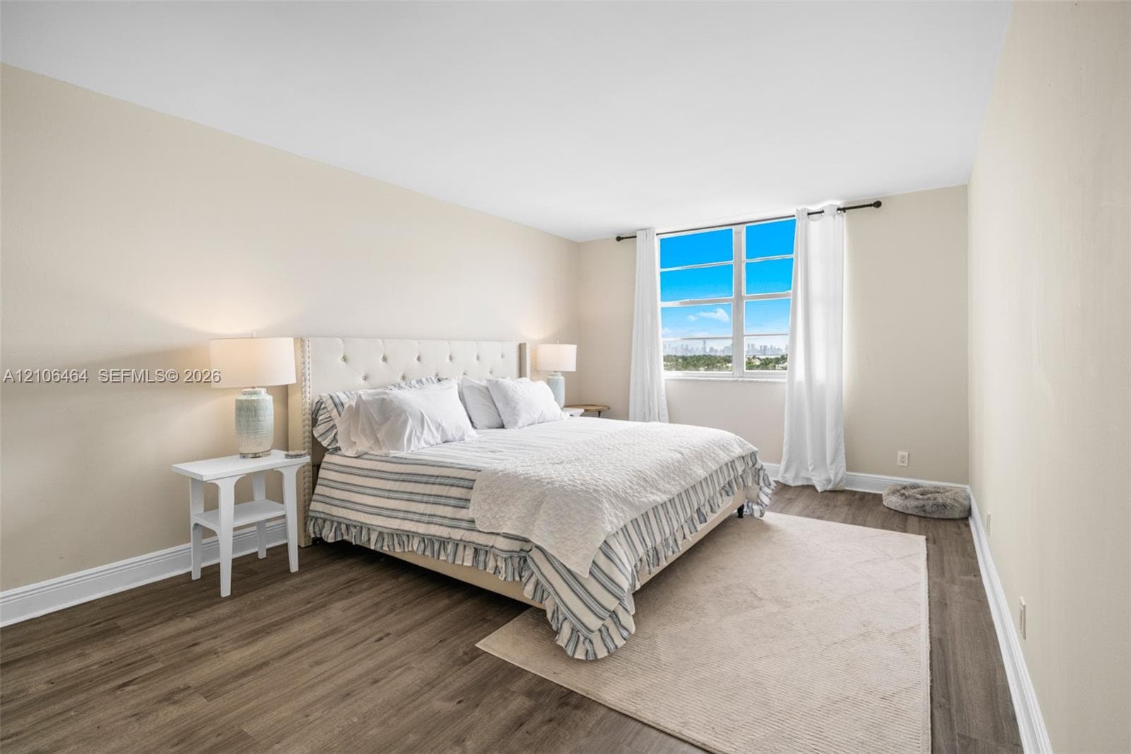 Neutral-toned bedroom featuring wood-finish flooring and large windows with natural lighting