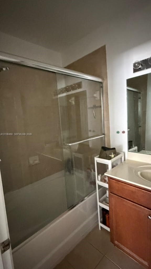 Bathroom featuring a tub-shower combination with sliding glass doors, neutral tile surround, wood-finish vanity cabinet, solid-surface countertop with an integrated sink, and an attached wall-mounted light fixture