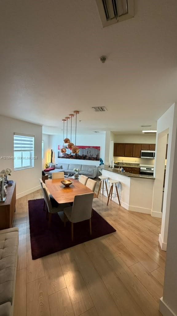 Open-concept layout featuring wood-finish flooring, multi-pendant lighting, and a kitchen peninsula with bar-top seating