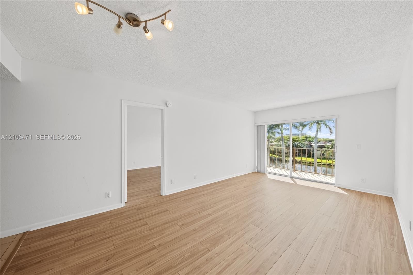 Open-concept room with wood-finish flooring, sliding glass doors to a balcony, and four-light adjustable track lighting