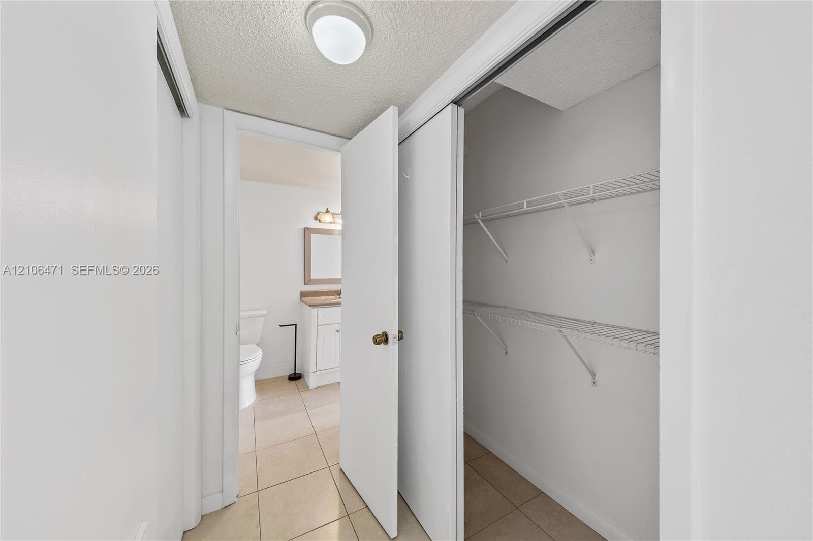 Built-in storage closet with tiered wire shelving and wide-swing door, featuring tile flooring and overhead dome lighting
