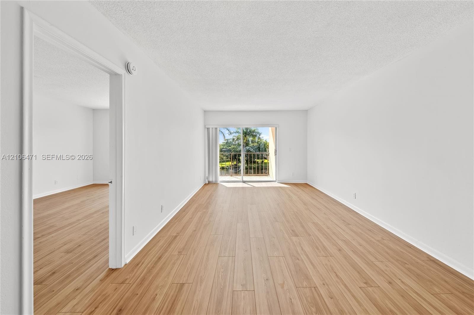 Neutral-toned interior featuring wood-finish flooring, white walls, and a sliding glass door opening to an exterior balcony