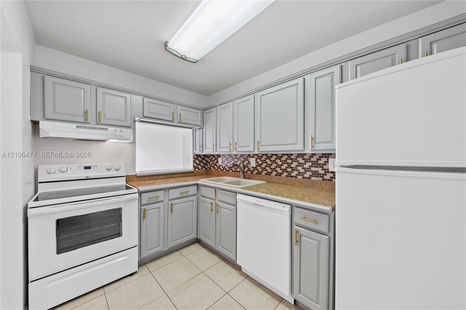 Kitchen featuring gray shaker-style cabinetry with gold-toned hardware, stone-finish countertops, a multi-tonal mosaic tile backsplash, and a double-basin sink