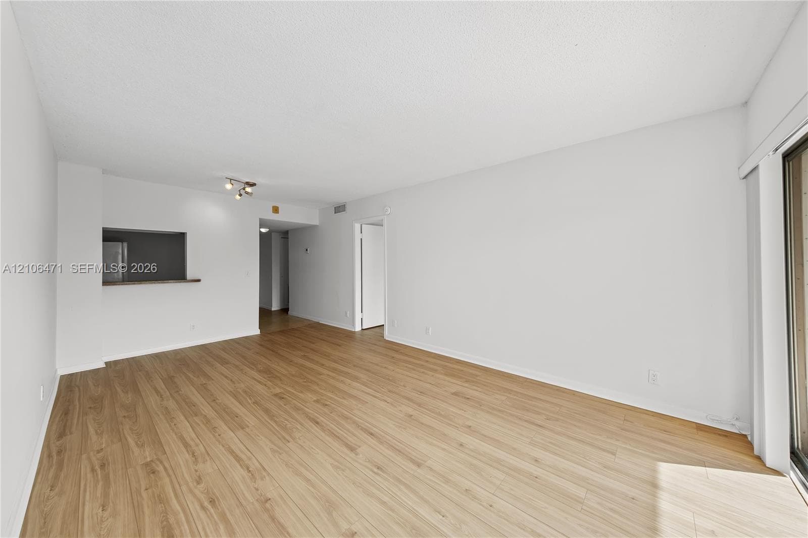 Neutral-toned living space featuring light wood-finish flooring, a pass-through opening, recessed lighting, and a sliding glass door