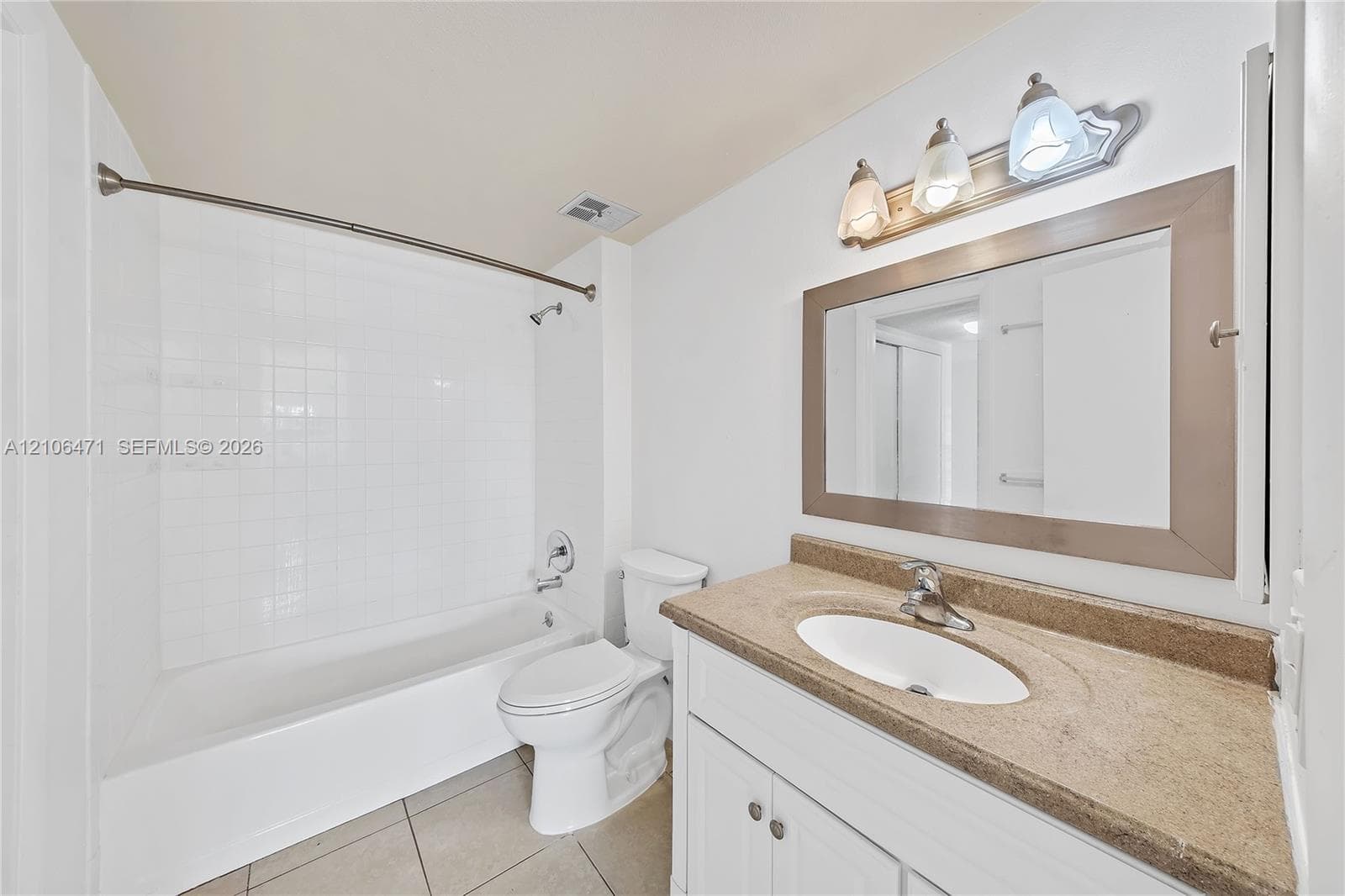 Bathroom featuring a tub-shower combination with white tile surround, vanity with an integrated sink and stone-finish countertop, framed wall mirror, and tri-light fixture