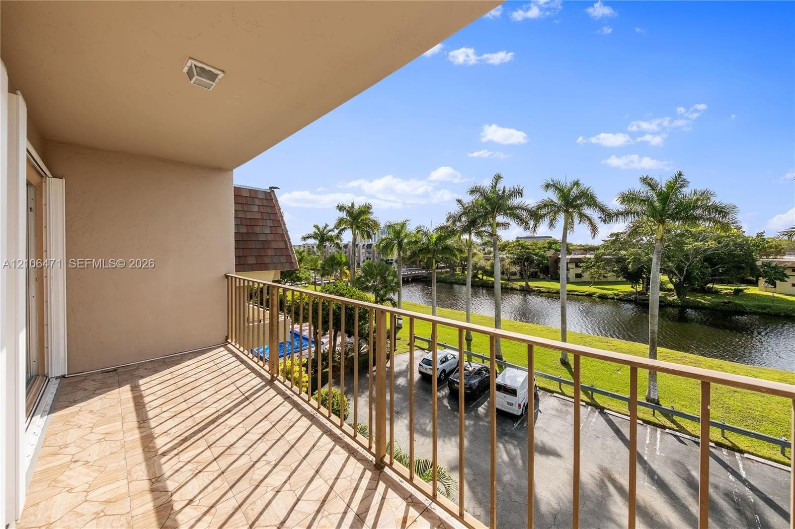 Covered balcony featuring tile flooring and metal railings overlooking a waterway and palm trees
