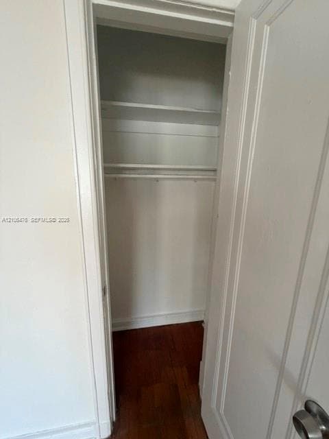 Reach-in closet featuring wood-finish flooring, white painted walls, and built-in shelving