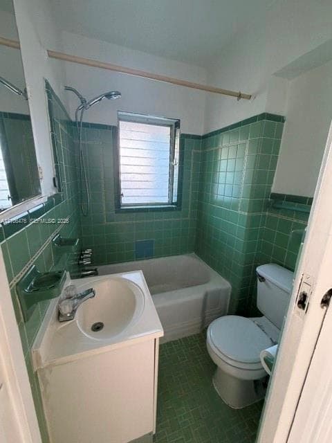 Bathroom featuring green ceramic wall and floor tiling, integrated bathtub and shower combination, vanity with an integrated basin, and louvered window