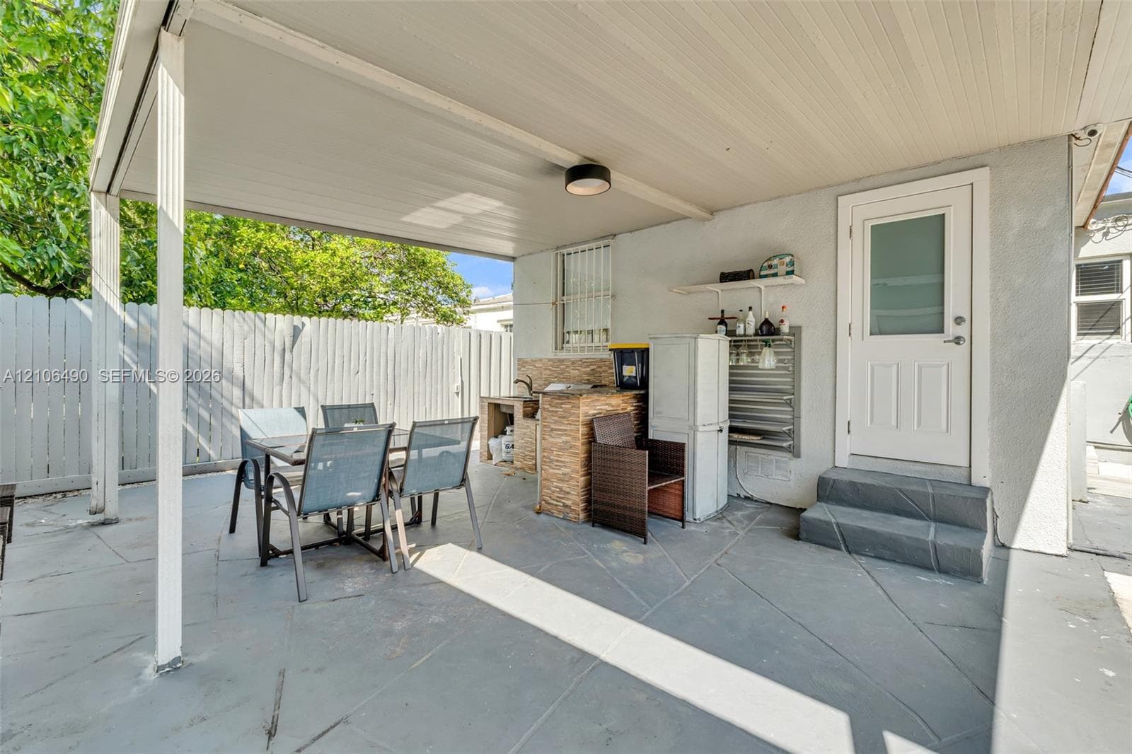 Covered patio featuring a paved floor, built-in outdoor kitchen with stone-veneer cladding, and perimeter wood fencing