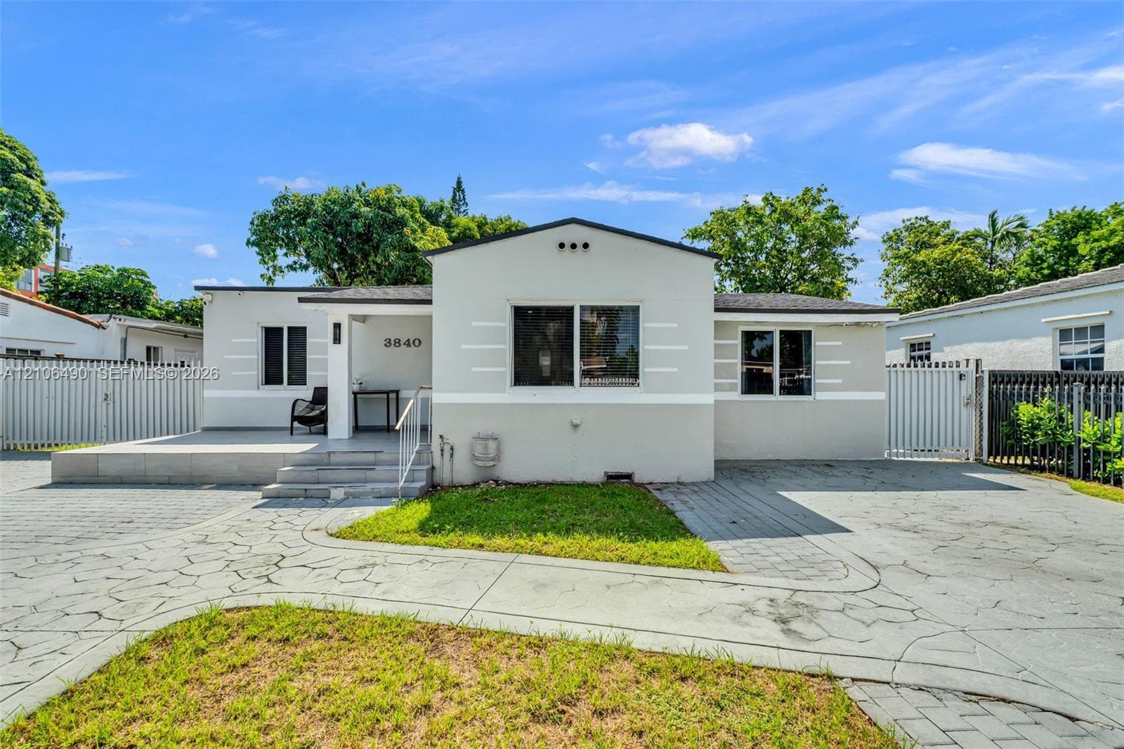 Stucco exterior featuring horizontal accent detailing, a covered front porch, patterned stone driveway, and perimeter fencing