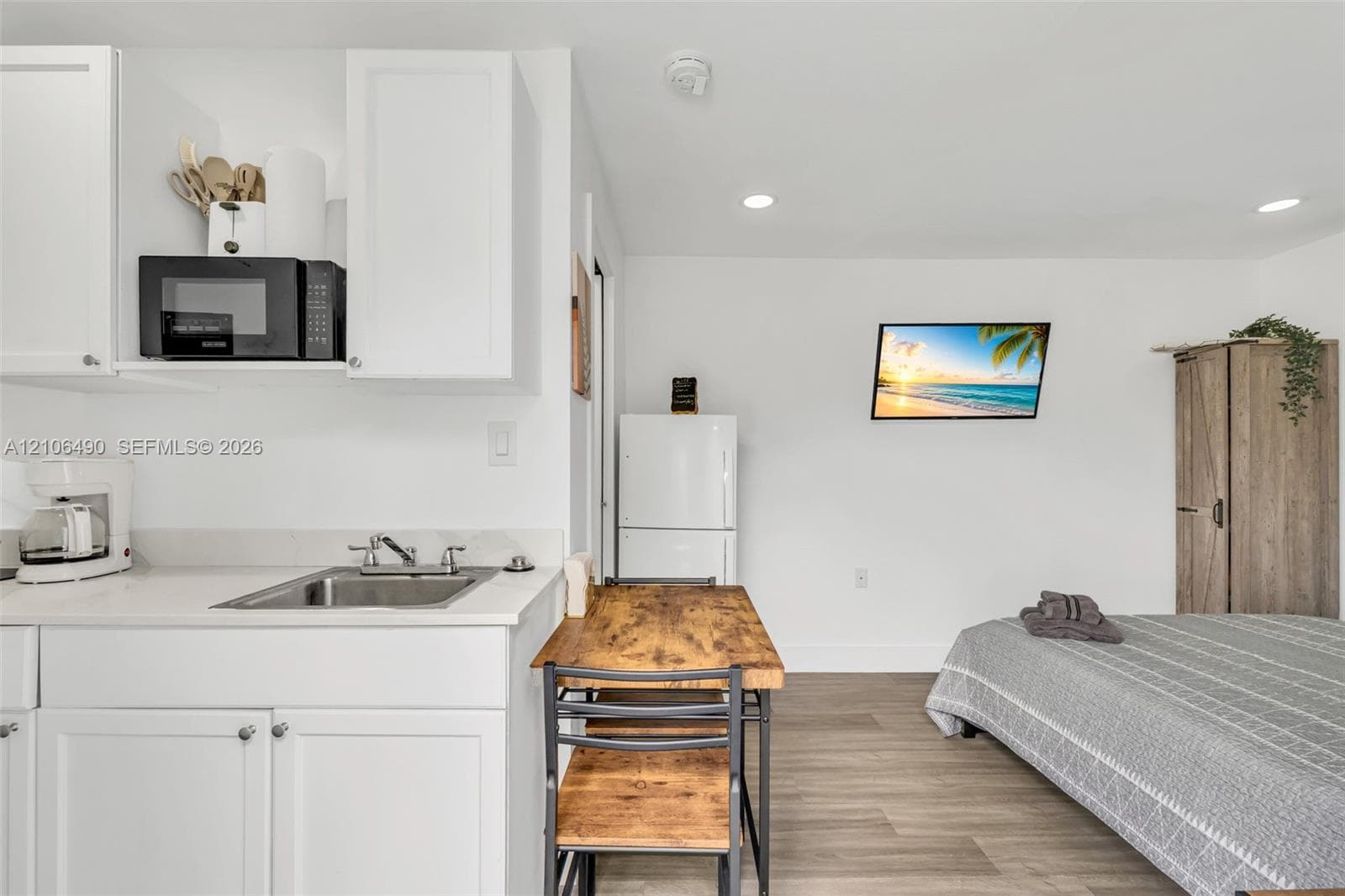 Kitchenette featuring white cabinetry, a stainless steel sink, solid-surface countertop, and recessed lighting with wood-finish flooring