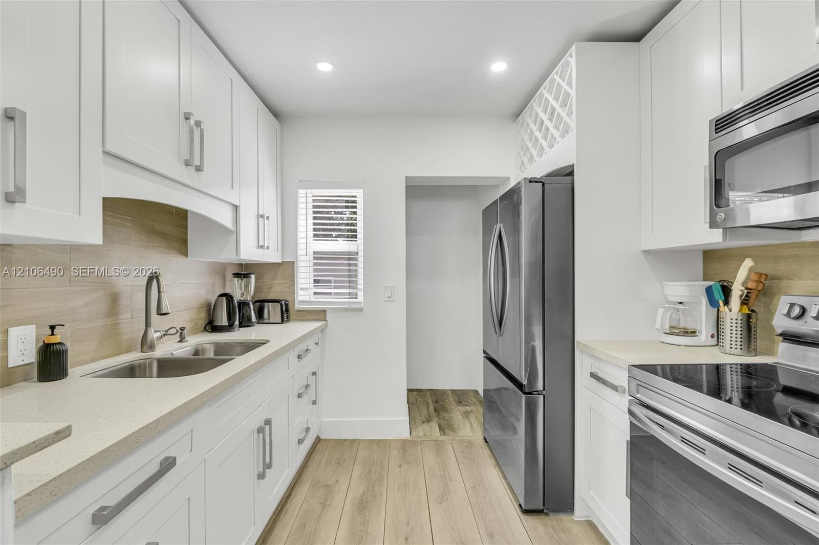 Kitchen featuring white shaker-style cabinetry, stainless steel appliances, neutral stone-finish countertops, tile backsplash, and wood-finish flooring