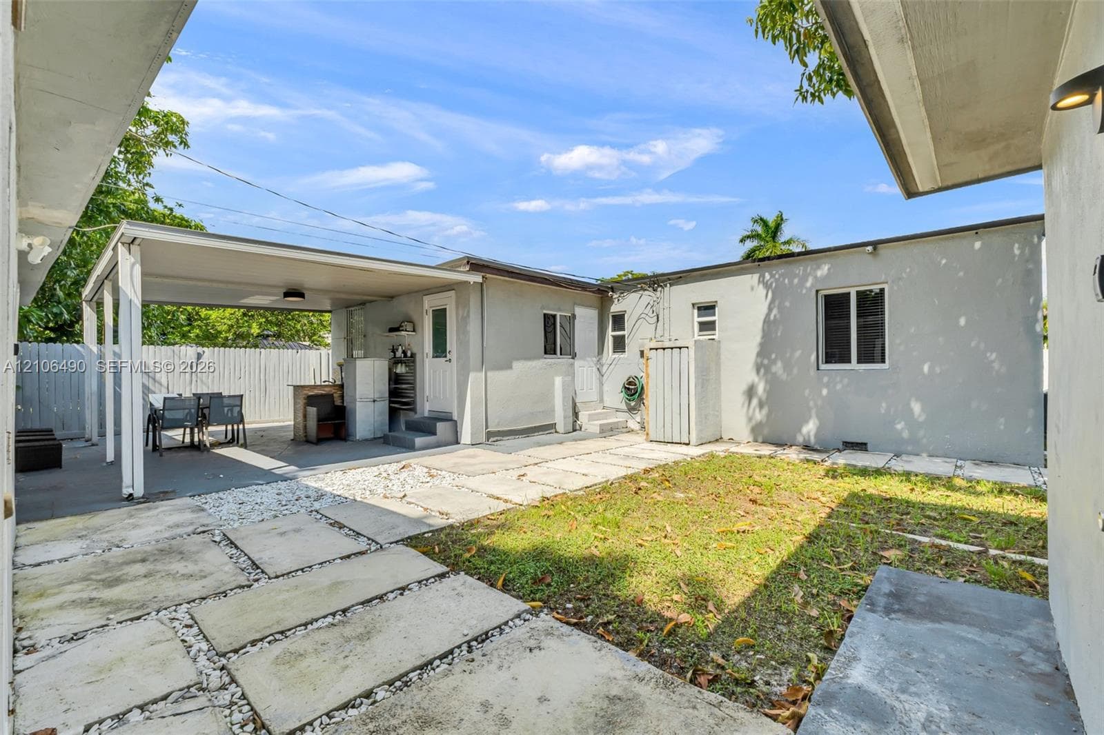 Backyard featuring a concrete-paver patio, covered porch, white wooden perimeter fencing, and an exterior built-in counter