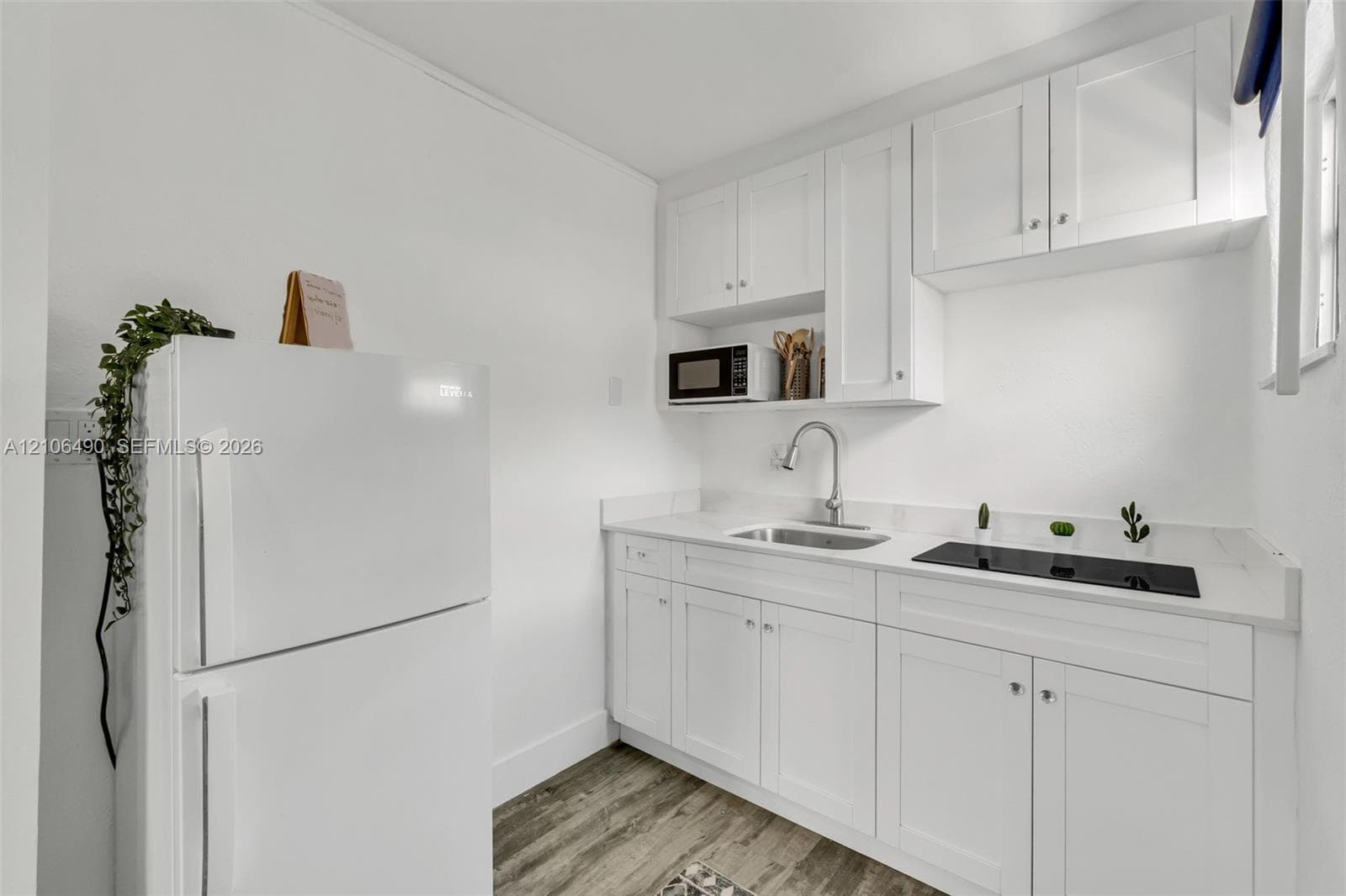 Kitchenette featuring white Shaker-style cabinetry, white countertops, built-in electric cooktop, stainless steel sink with high-arc faucet, and wood-finish flooring