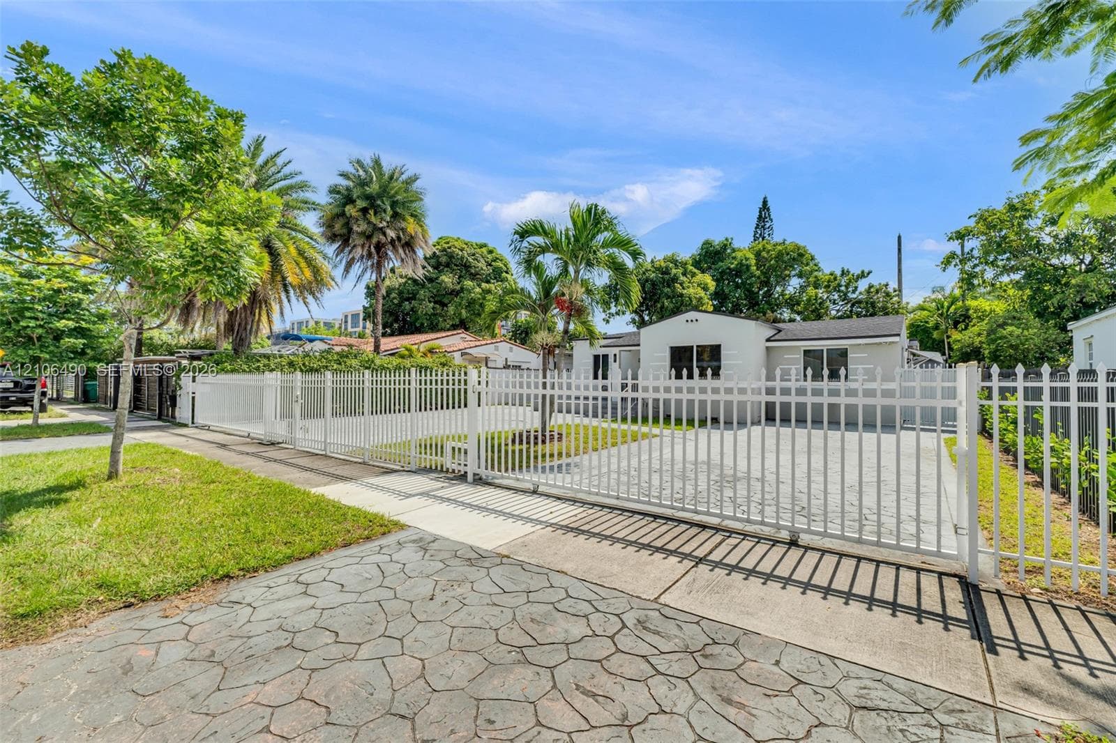 Exterior featuring white stucco facade, stamped concrete driveway, and full-perimeter white metal fencing with sliding gate