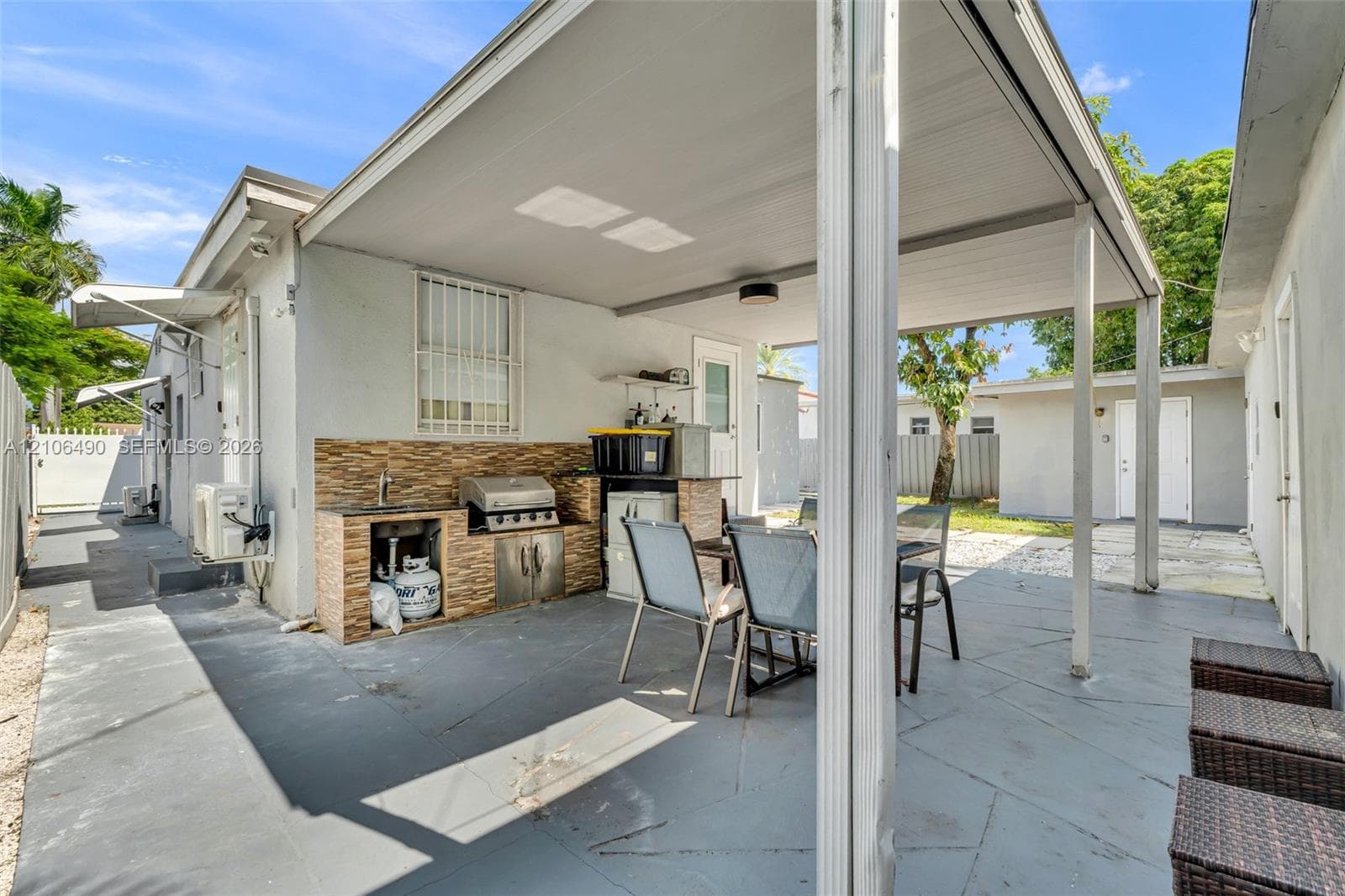 Covered patio featuring a built-in outdoor kitchen with stone-finish tiling, a stainless steel grill, a sink, and concrete flooring