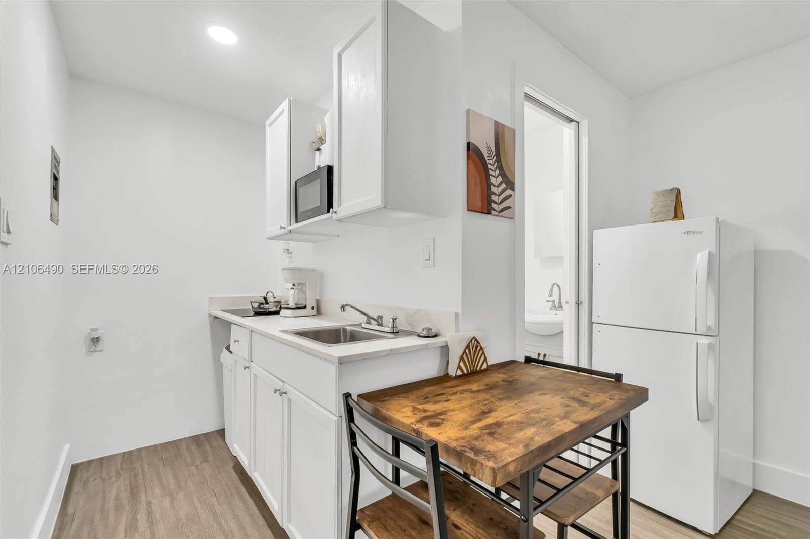 Compact kitchenette featuring white cabinetry, a stainless steel sink with a metallic faucet, a built-in microwave, and wood-finish flooring