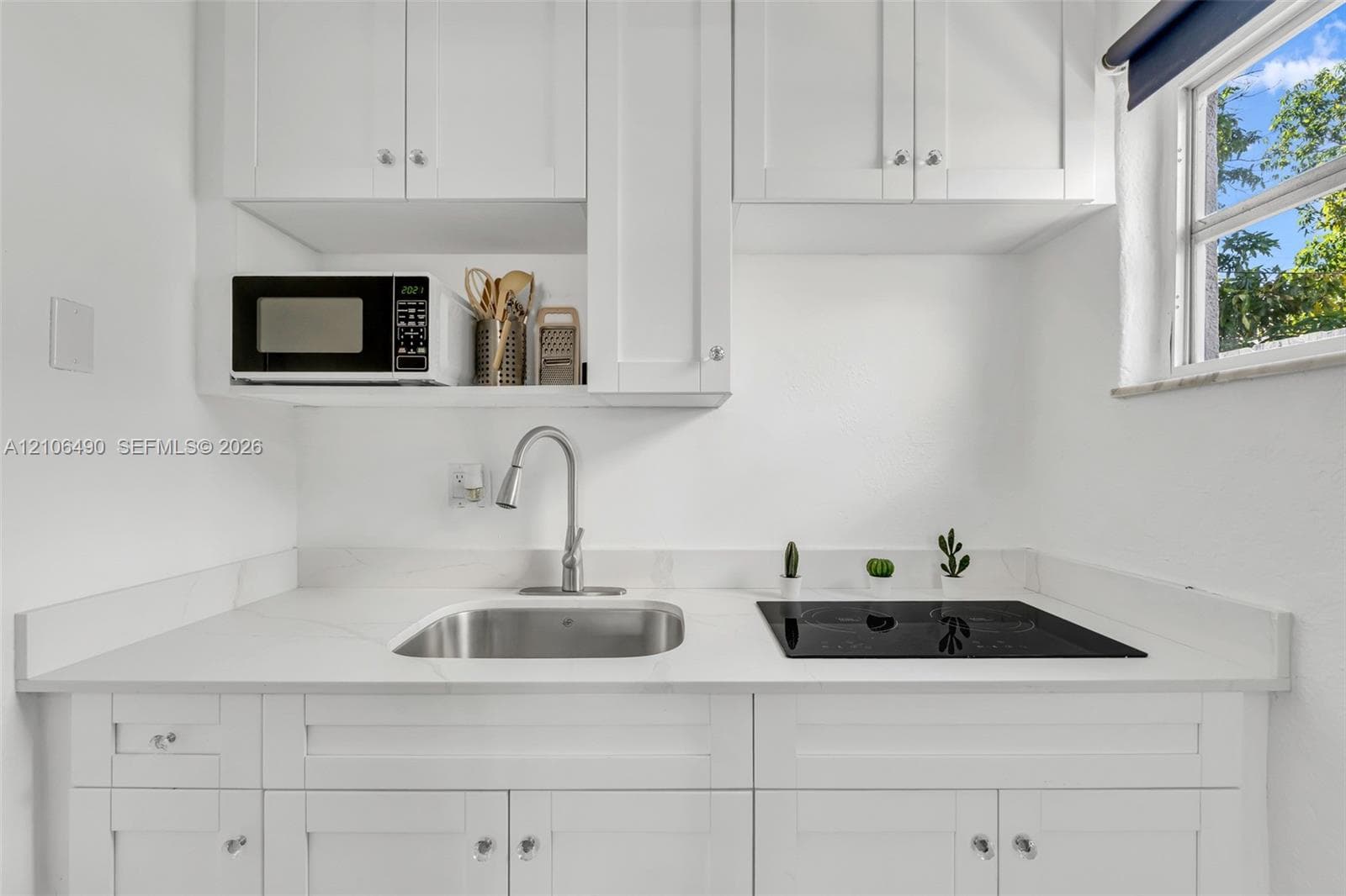 White shaker-style cabinetry, quartz countertop, stainless steel drop-in sink, chrome gooseneck faucet, and built-in electric cooktop